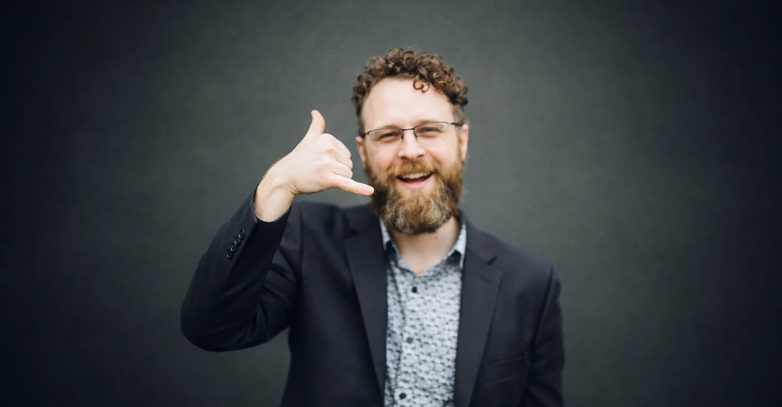 Kelowna realtor Byron Armstrong gesturing a phone call sign inviting clients to contact him for real estate services.